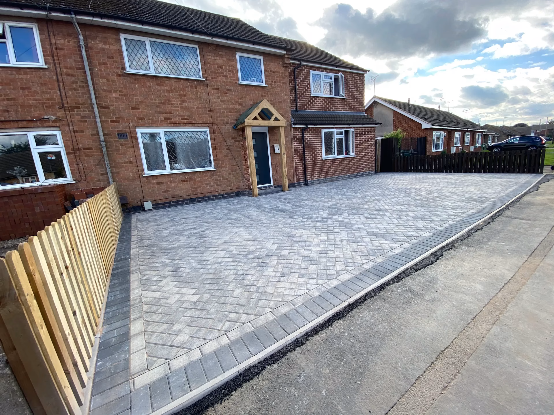 Grey block-paved driveway with charcoal edging outside a red-brick home