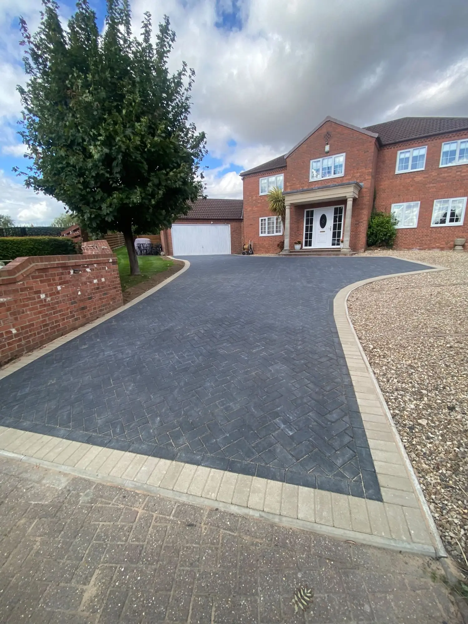 Charcoal herringbone block-paved driveway curving up to the double garage of a detached house in Tuxford