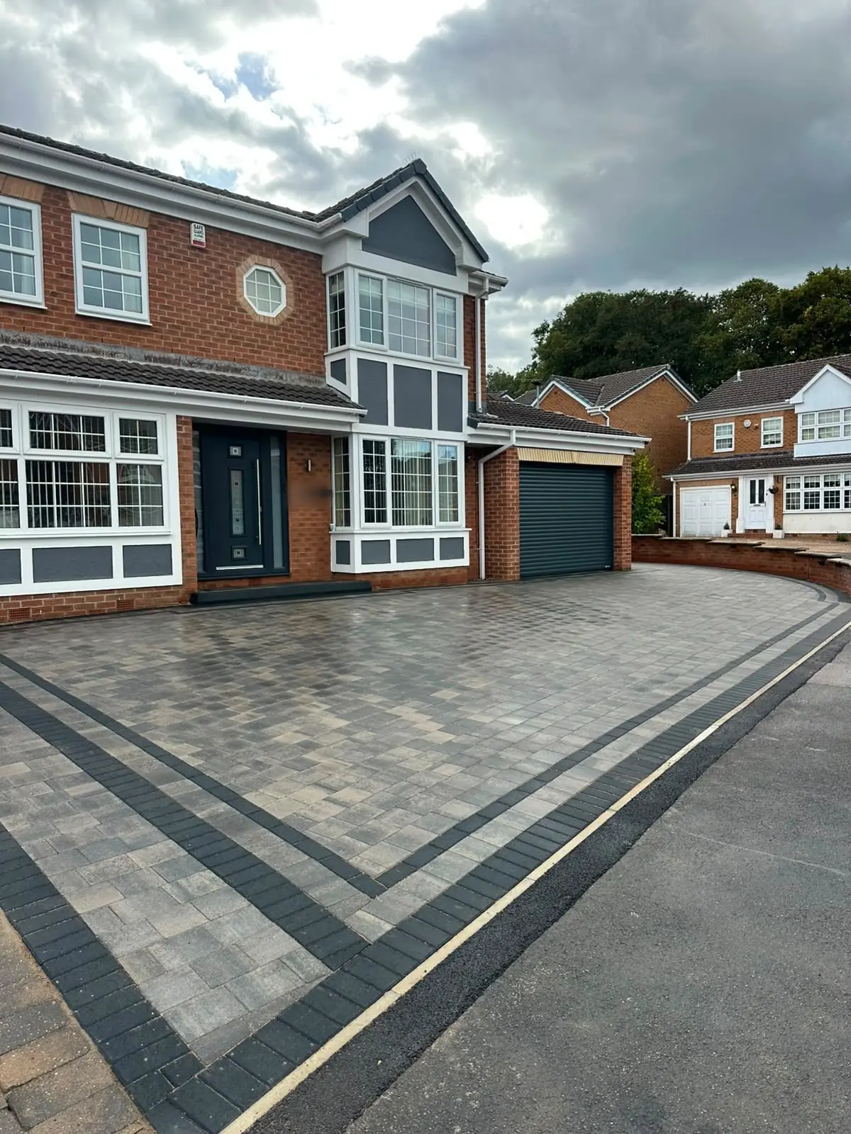 Slate grey block paving with charcoal border lines leading to the front door and roller garage of a house in Todwick
