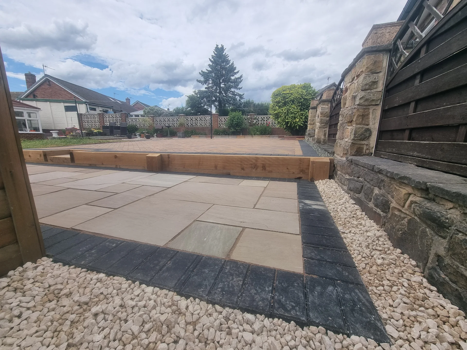 Sandstone patio with a charcoal block border and white pebble edging in a back garden