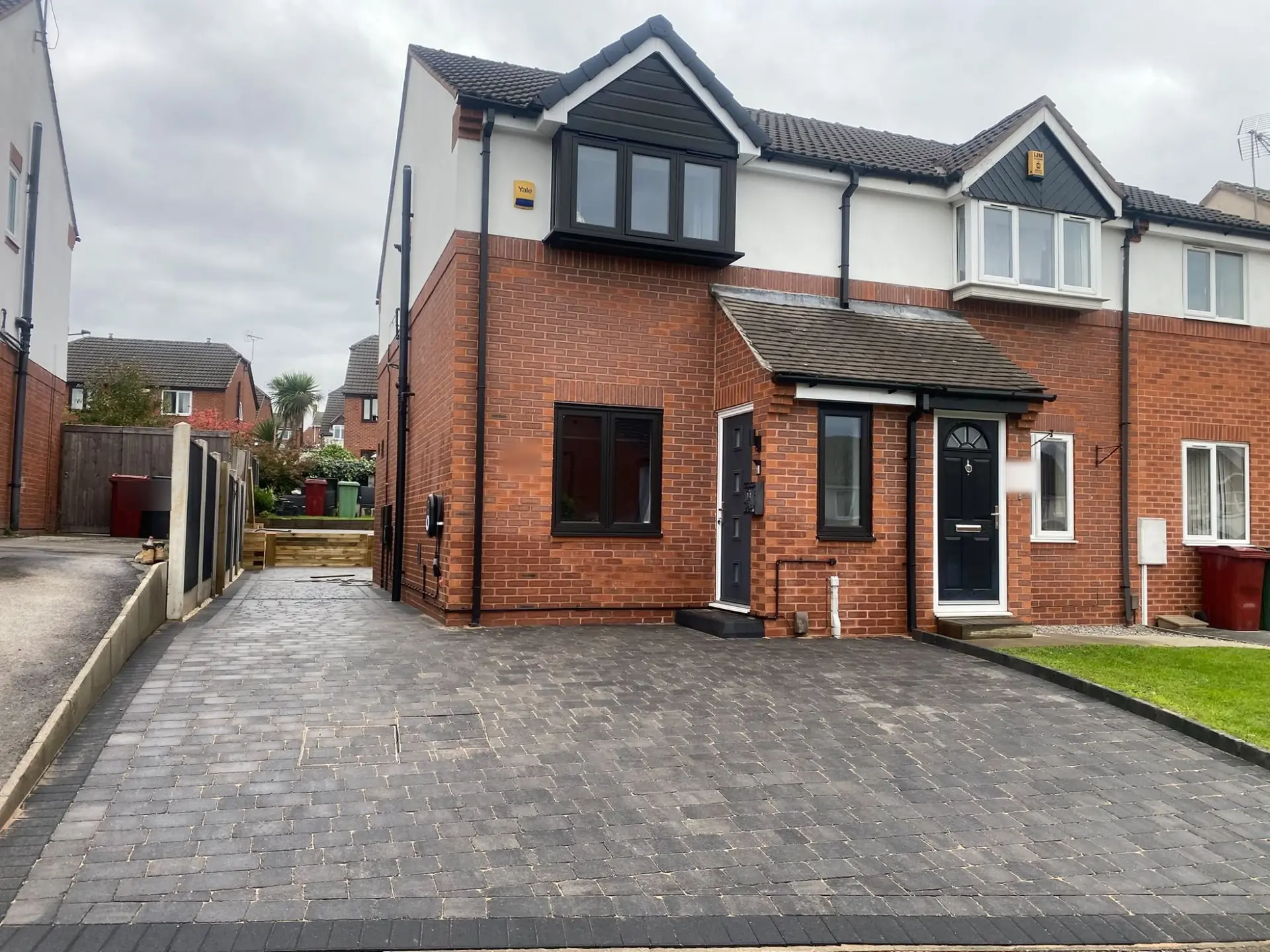 Dark charcoal Tegula block paving with a charcoal block edge outside a red-brick semi-detached house