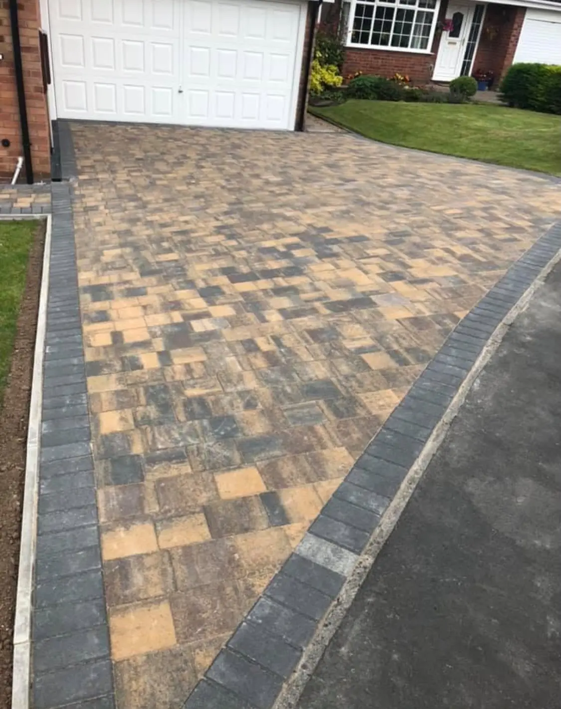 Golden brown and charcoal Tegula block paving with a charcoal block border between a lawn and the road