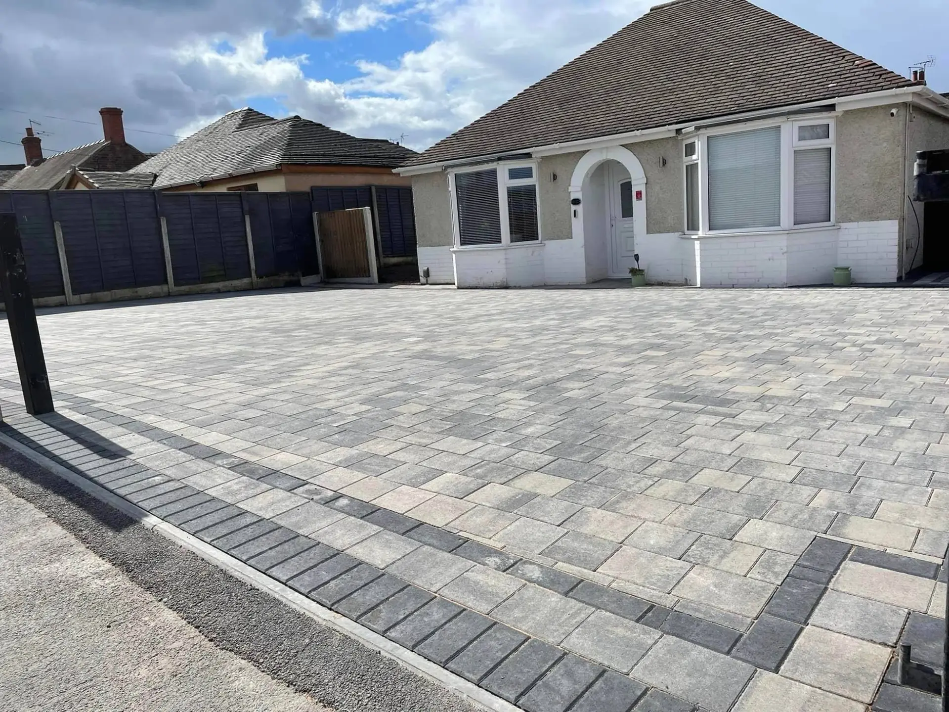 Wide driveway in grey and charcoal block paving with a charcoal border in front of a bungalow