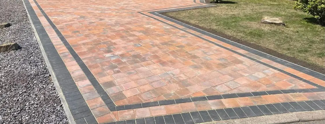 Orange and charcoal Tegula block paving with a double charcoal block border beside slate chippings and a lawn