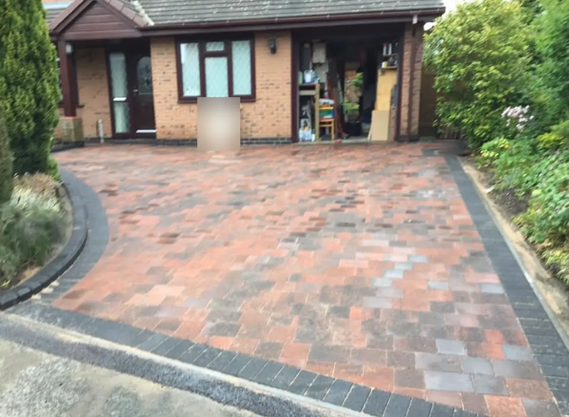 Red and charcoal Tegula block paving with a curved charcoal block border in front of a brick bungalow