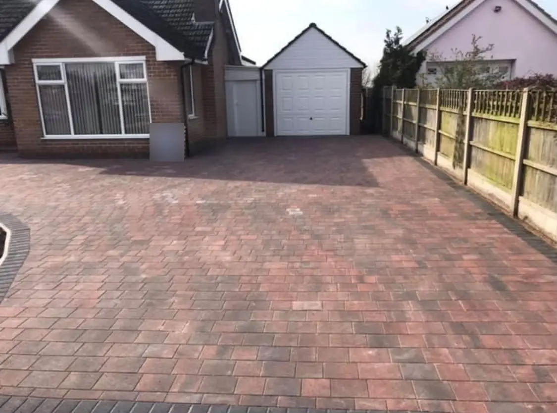 Tegula block paving driveway in red and charcoal tones leading to a detached garage beside a brick bungalow