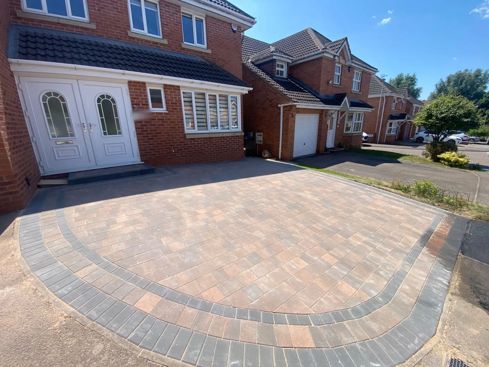 Red and brown Tegula block paving with a curved charcoal block border outside a red-brick detached house