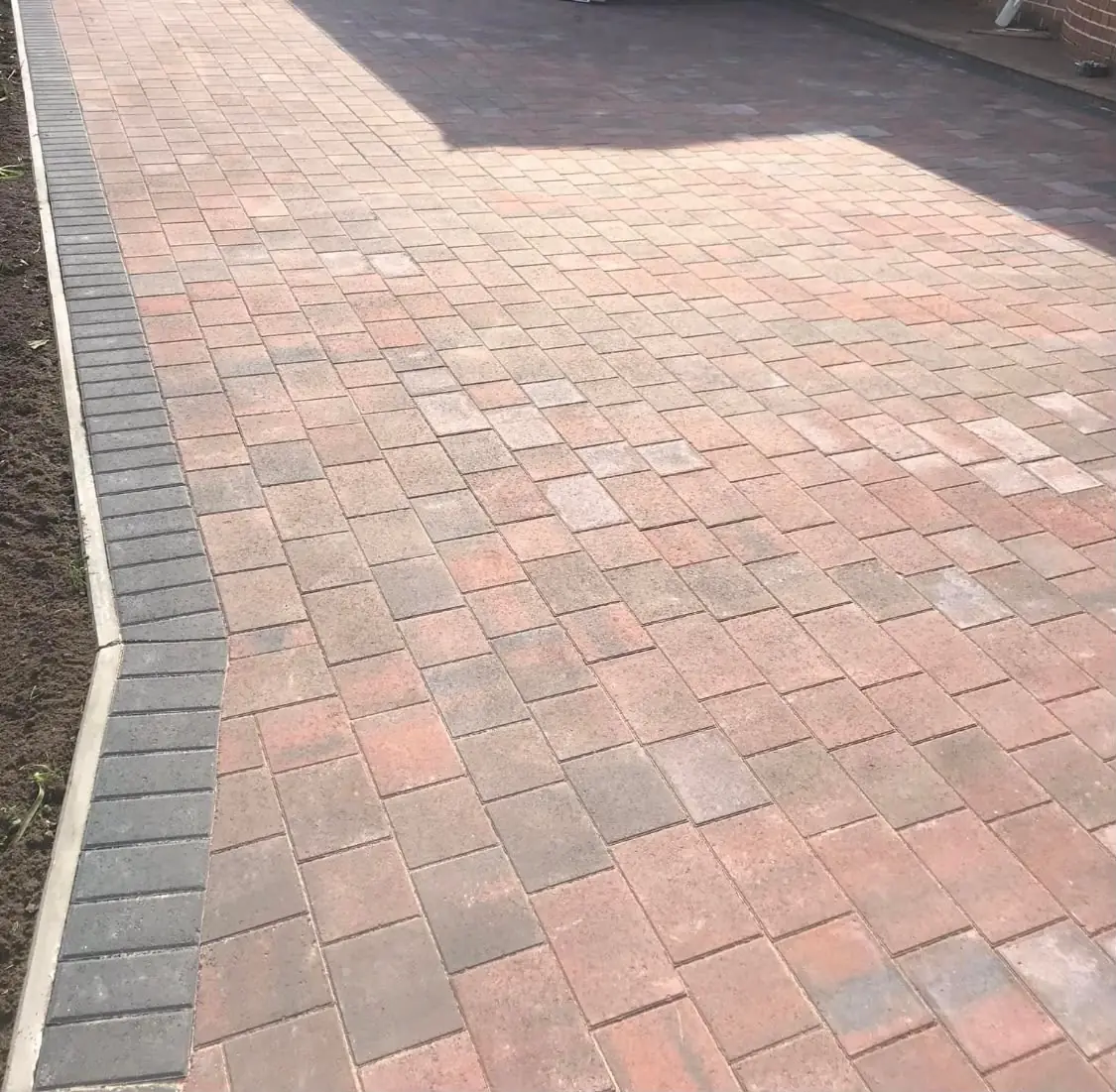 Red and grey Tegula block paving laid to a charcoal block edge beside freshly dressed soil