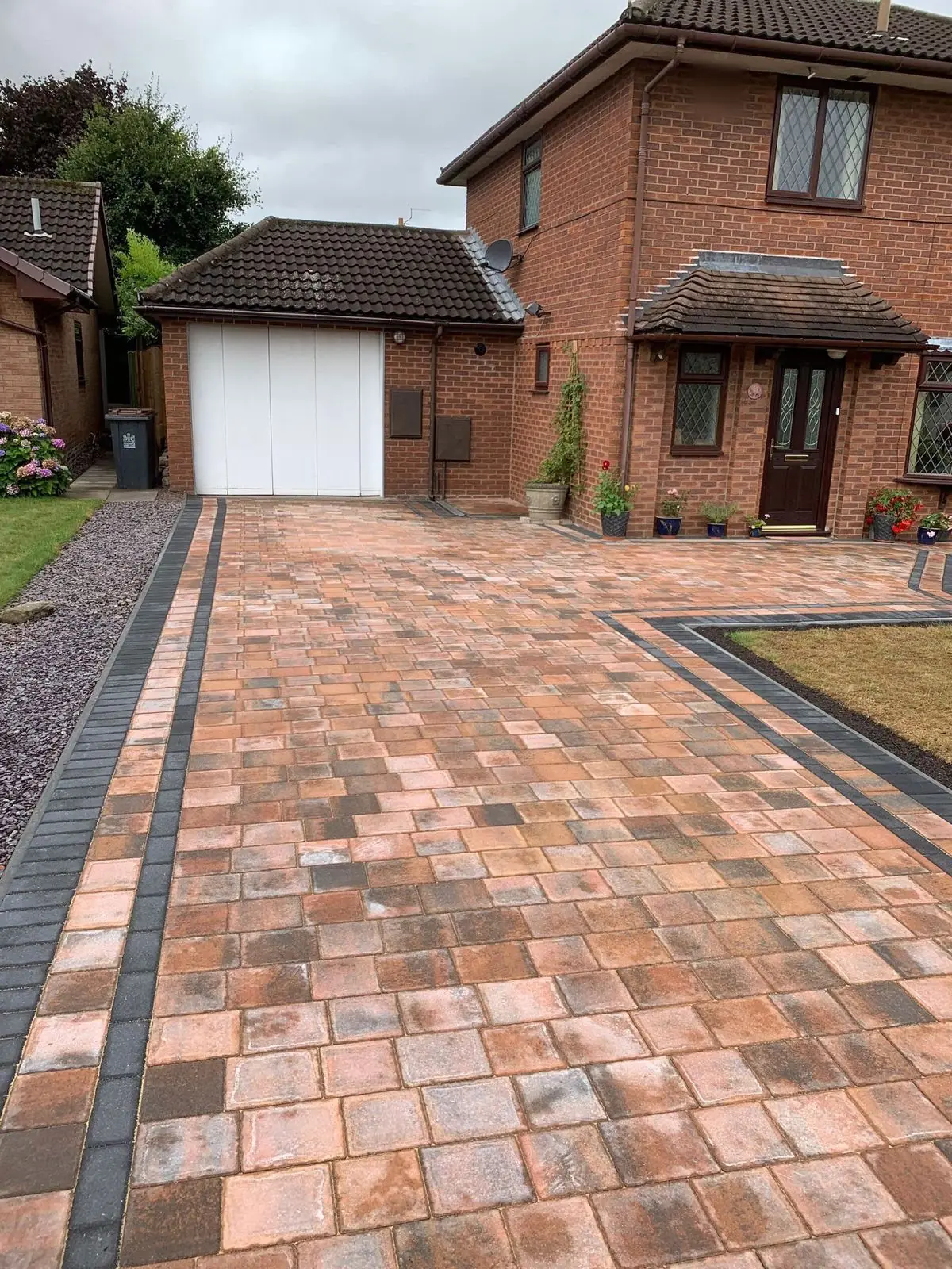 Red, orange and brown Tegula block paving with a charcoal block border leading to a garage
