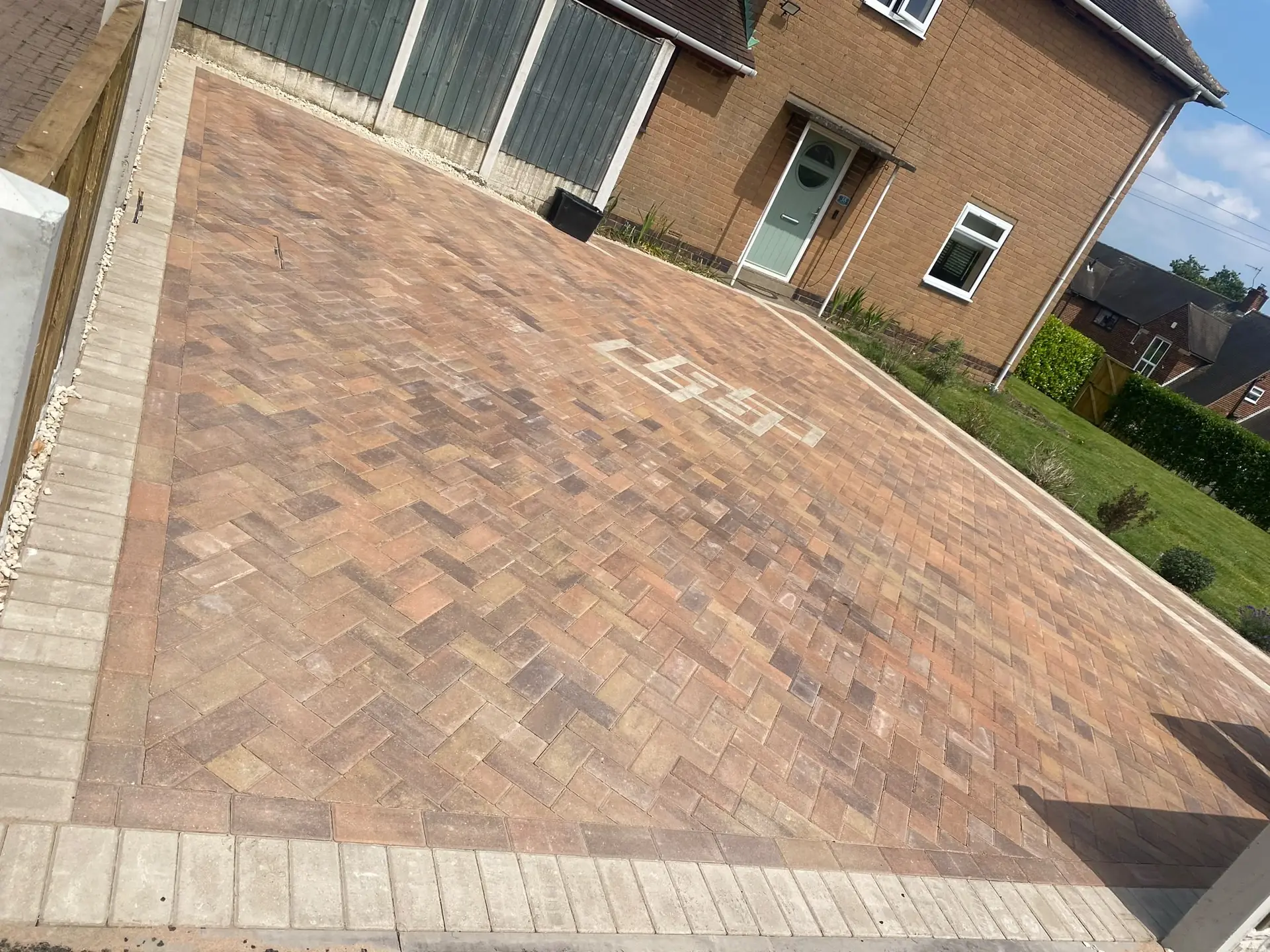 Multi-tone herringbone block paving with a buff border and a patterned inlay