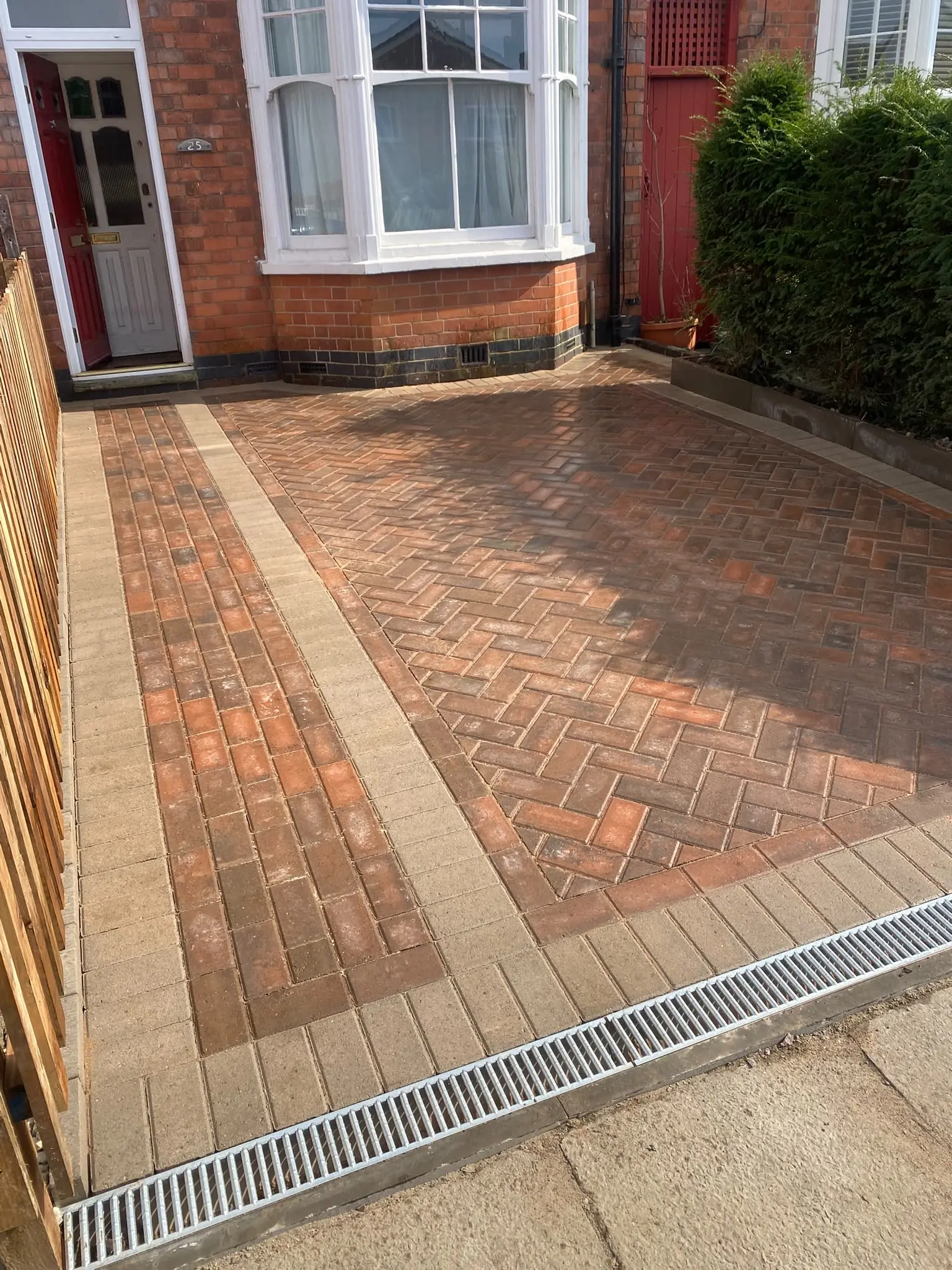 Red herringbone block paving with buff border and a channel drain across the entrance