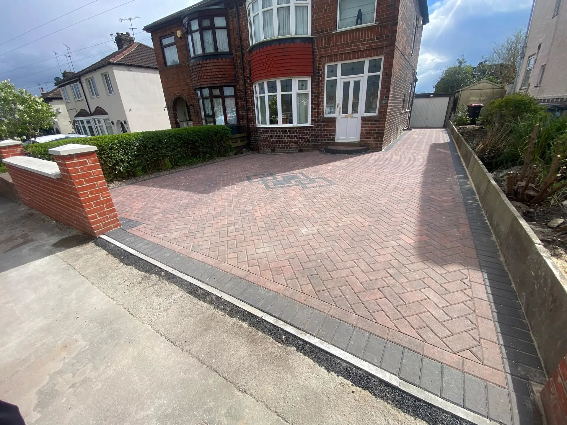 Red herringbone block paving with a charcoal border and a small feature inlay