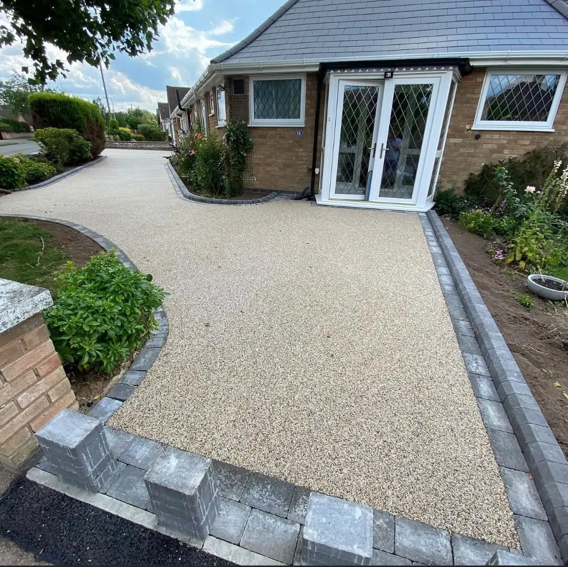 Beige resin bound driveway curving round a bungalow with a charcoal block border